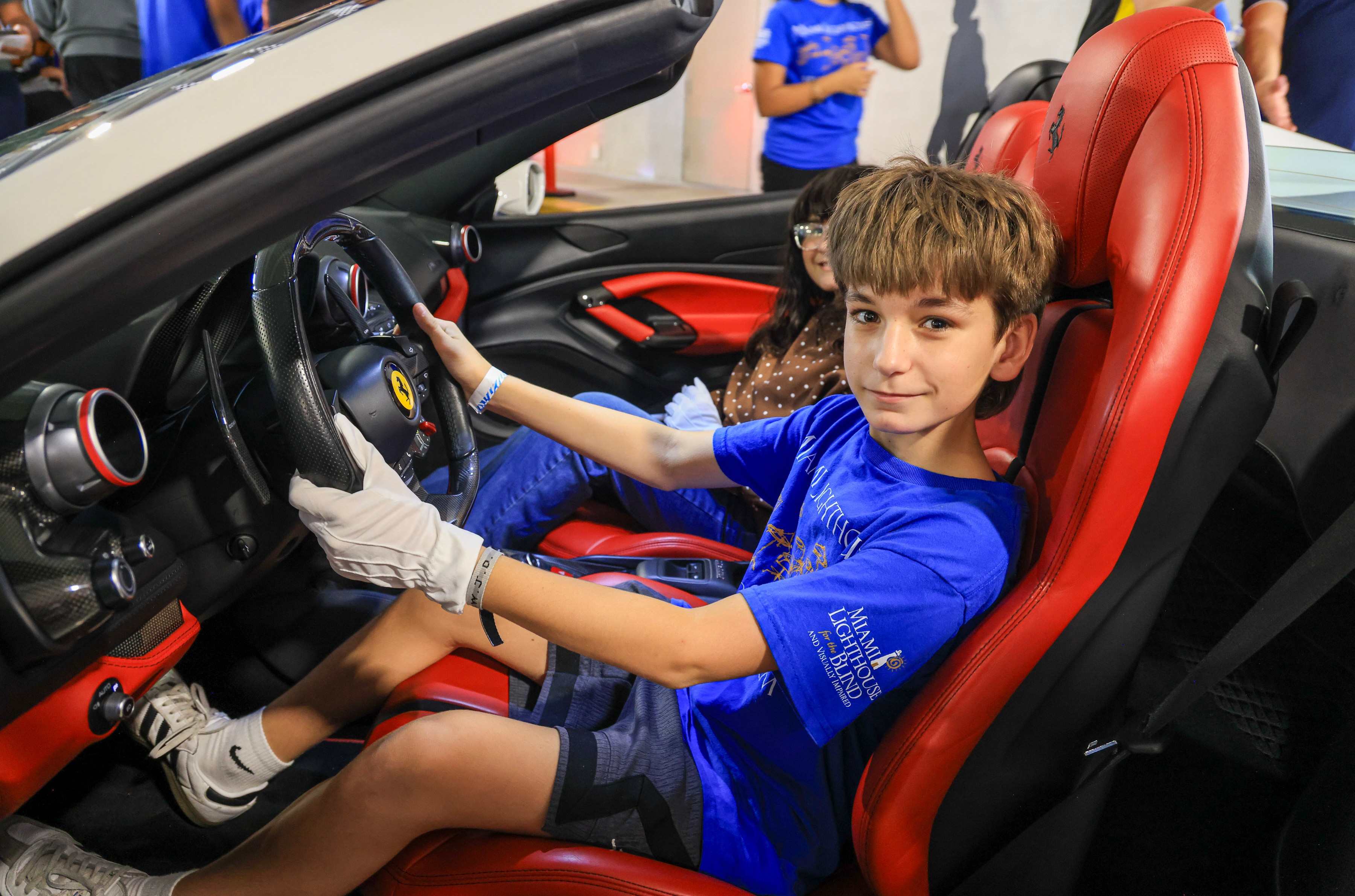 Un estudiante de Miami Lighthouse con camiseta azul y guantes blancos al volante de un Ferrari de asientos rojos