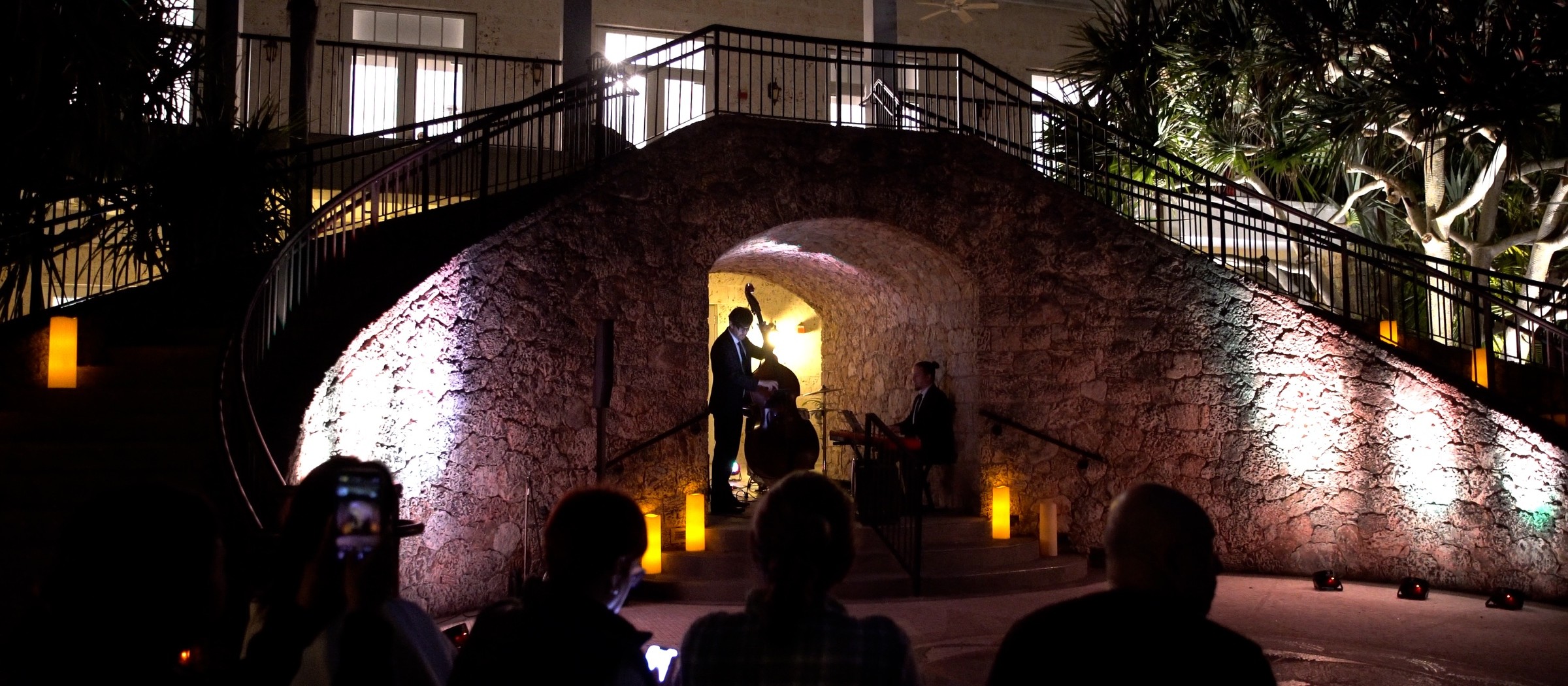 A jazz band playing under a lit stone archway at night, the audience in silhouette