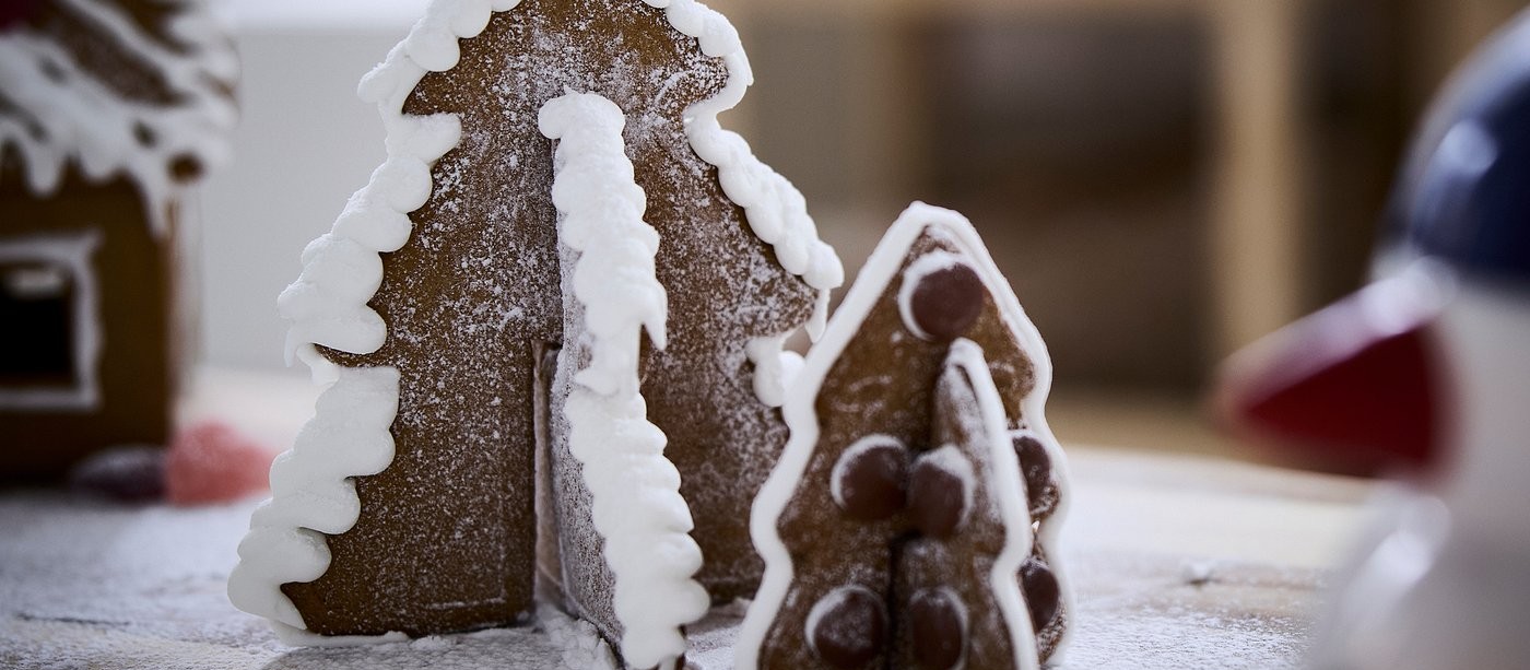 Gingerbread trees with white icing on a table dusted with powdered sugar