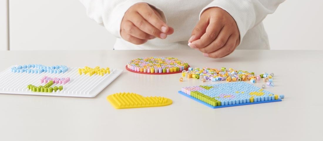 A child building a design from colorful PYSSLA beads on a pegboard