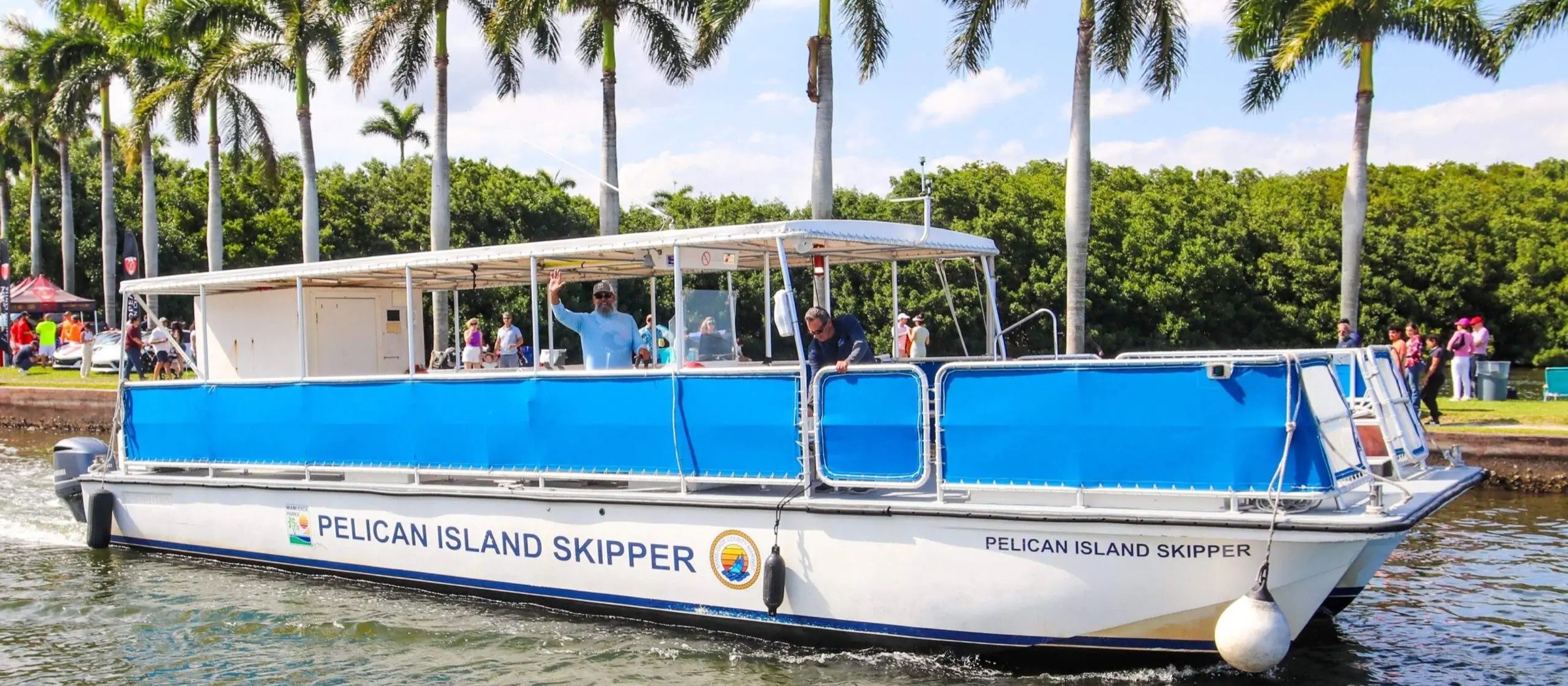 El catamarán Pelican Island Skipper con pasajeros navegando frente a las palmeras del Deering Estate
