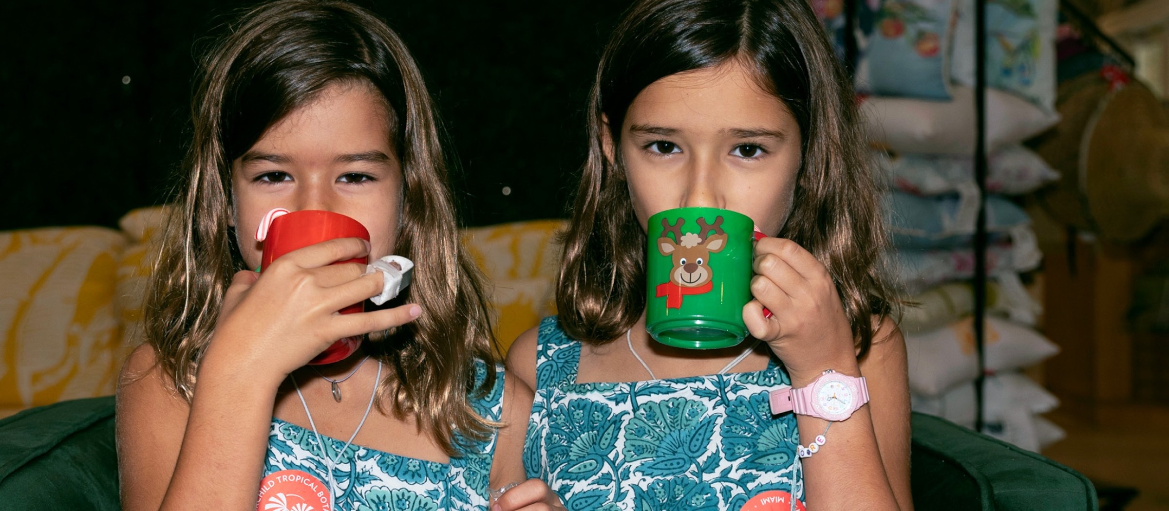 Dos niñas con vestidos iguales tomando de tazas navideñas y sosteniendo una hoja de actividades