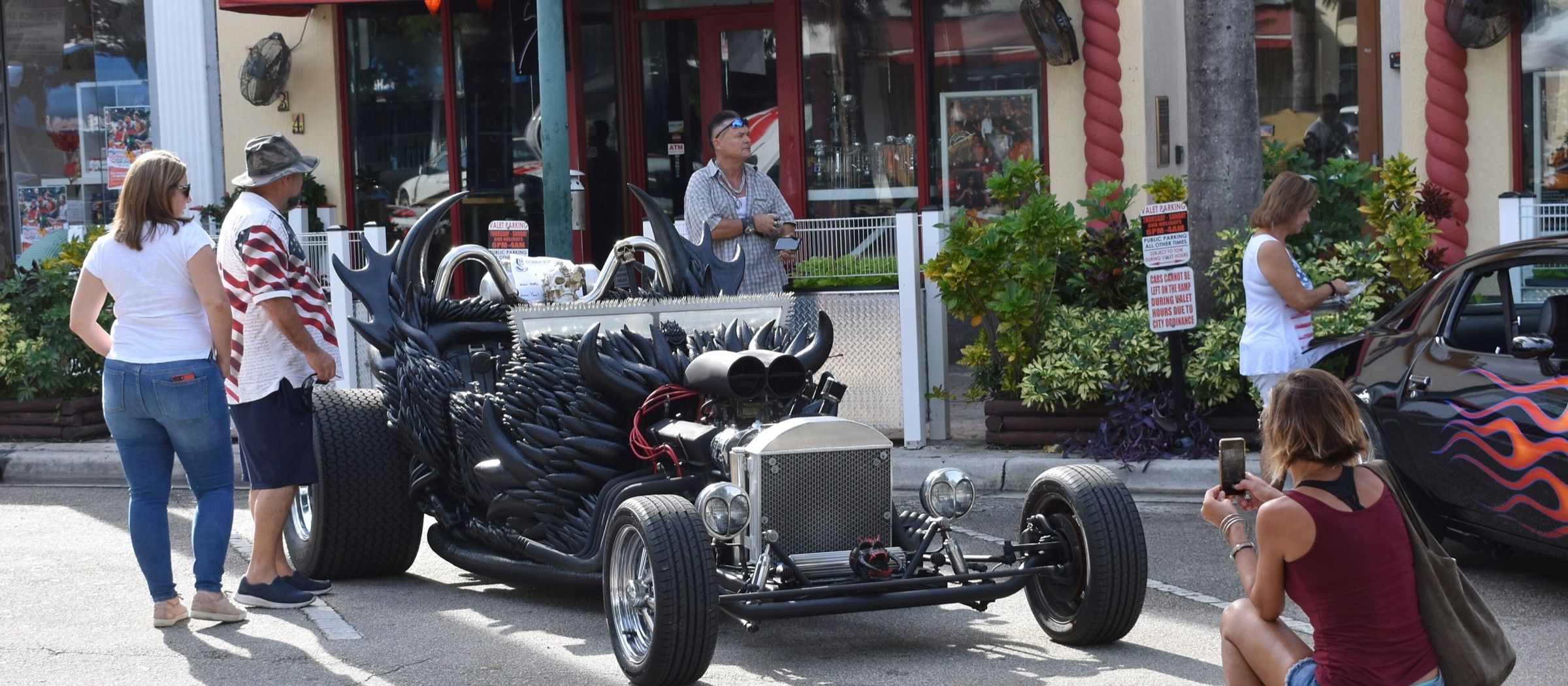 Un hot rod negro con llamas pintadas estacionado en Hollywood Boulevard mientras los visitantes lo miran