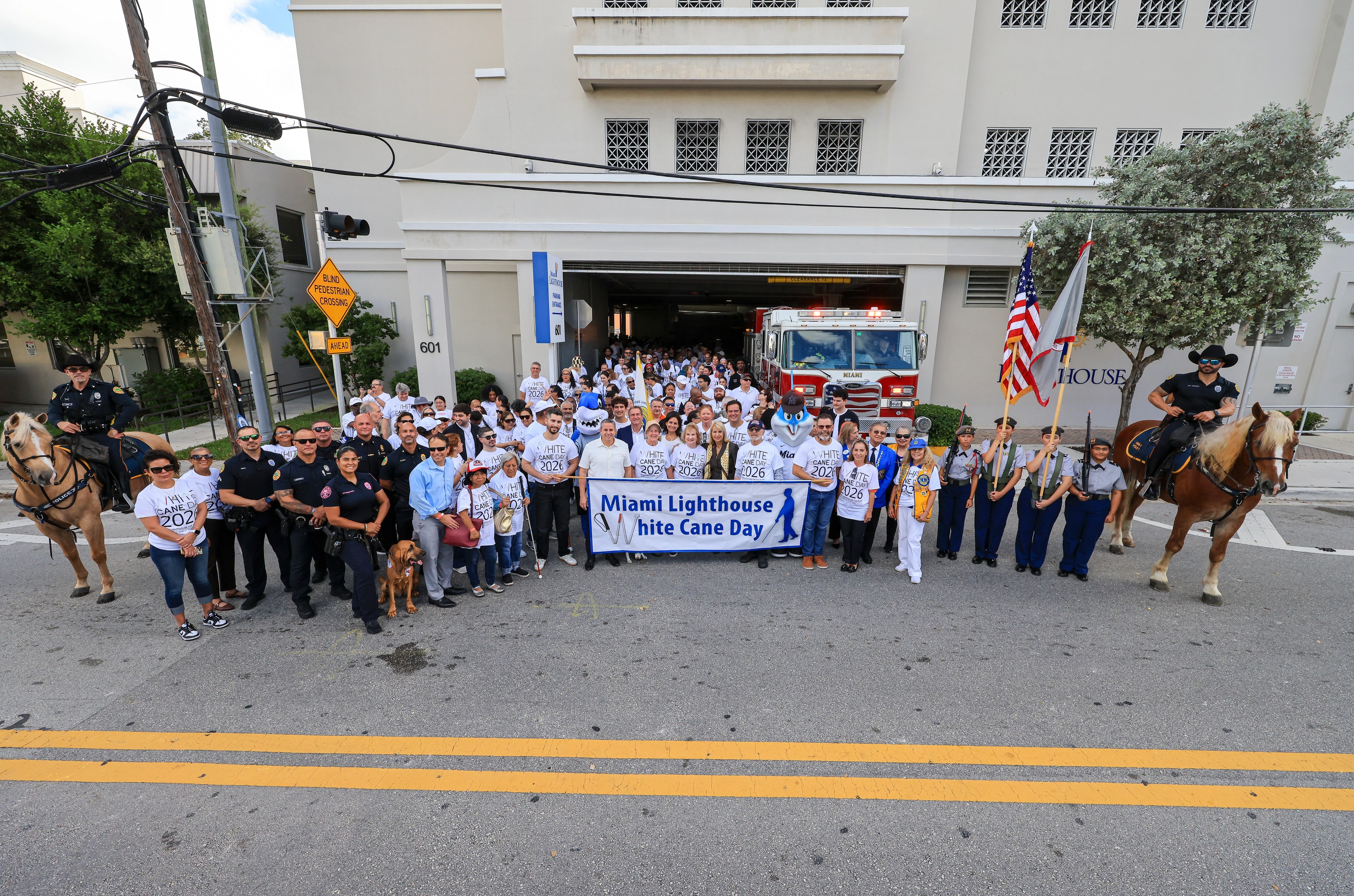 White Cane Day walkers in matching T-shirts behind a Miami Lighthouse banner, with mounted police officers on both sides