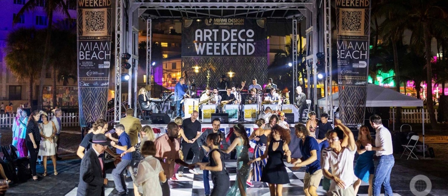 Gente bailando sobre un piso a cuadros frente al escenario Jazz Age Stage de Art Deco Weekend de noche