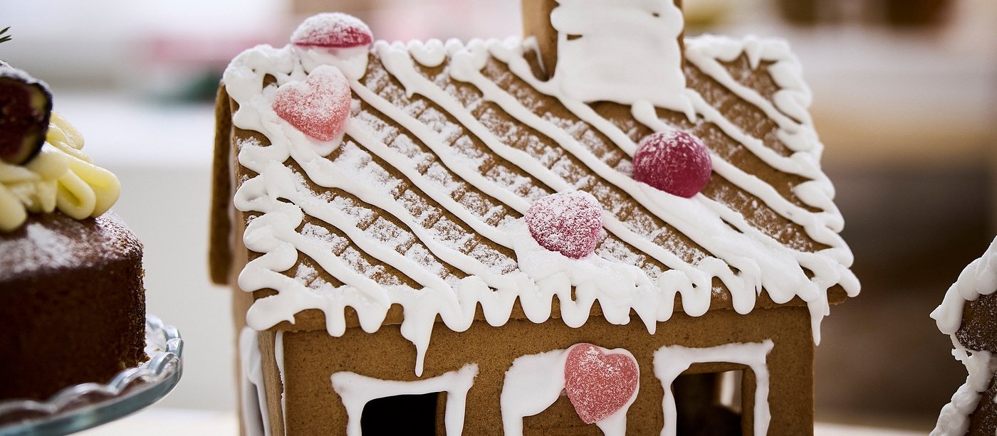 A gingerbread house with white icing and pink candy hearts on its roof