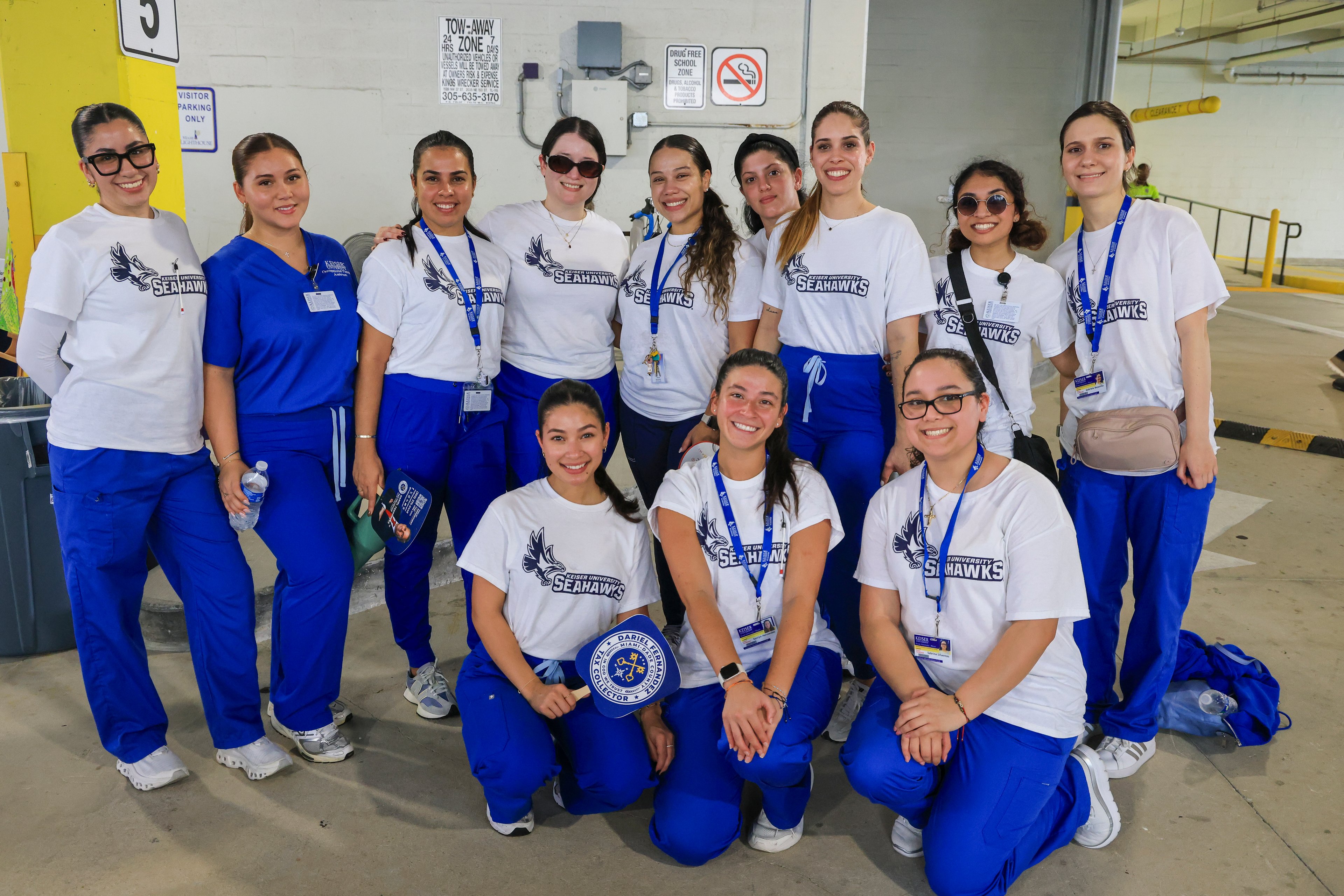 Doce voluntarios de Keiser University con camisetas de los Seahawks y uniformes médicos azules en un estacionamiento
