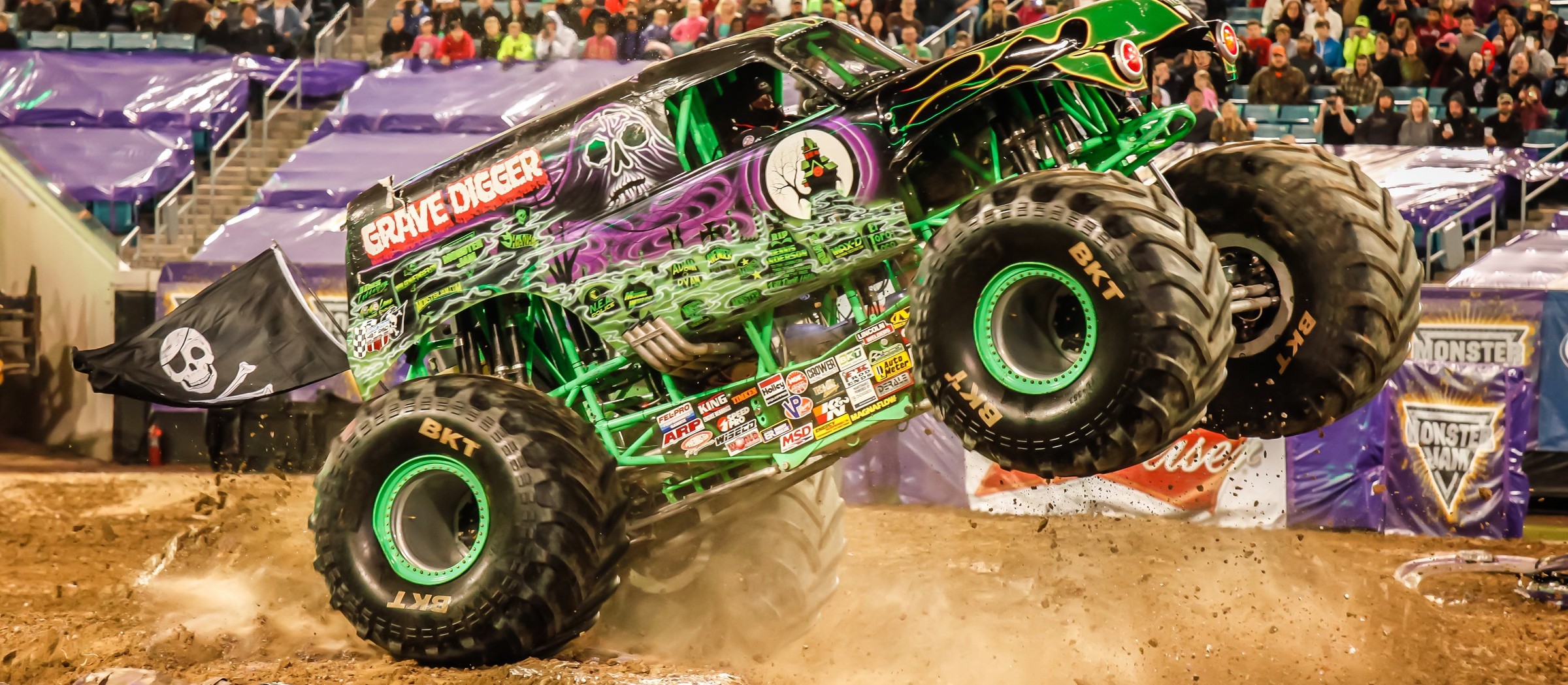 The Grave Digger monster truck jumps over a dirt ramp in a packed stadium