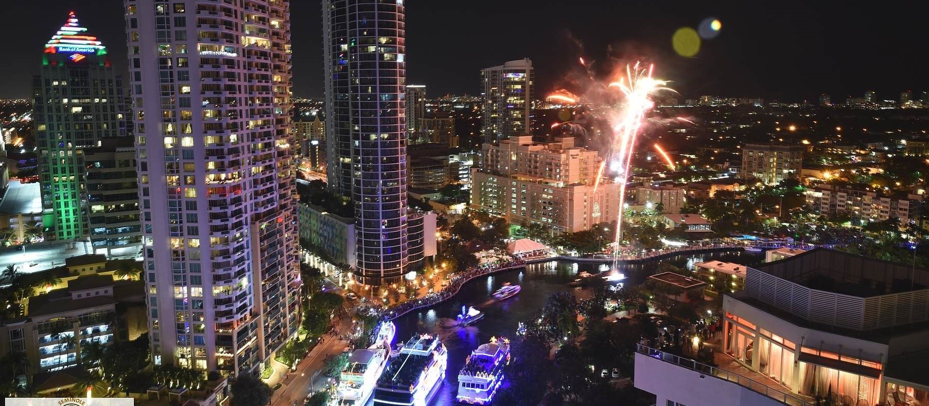 Barcos iluminados en el New River, en el centro de Fort Lauderdale, de noche, con fuegos artificiales sobre los edificios