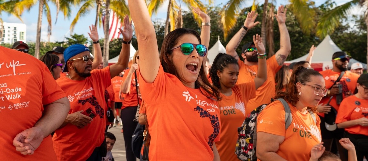 Walkers in orange Heart Walk shirts cheering with their arms raised