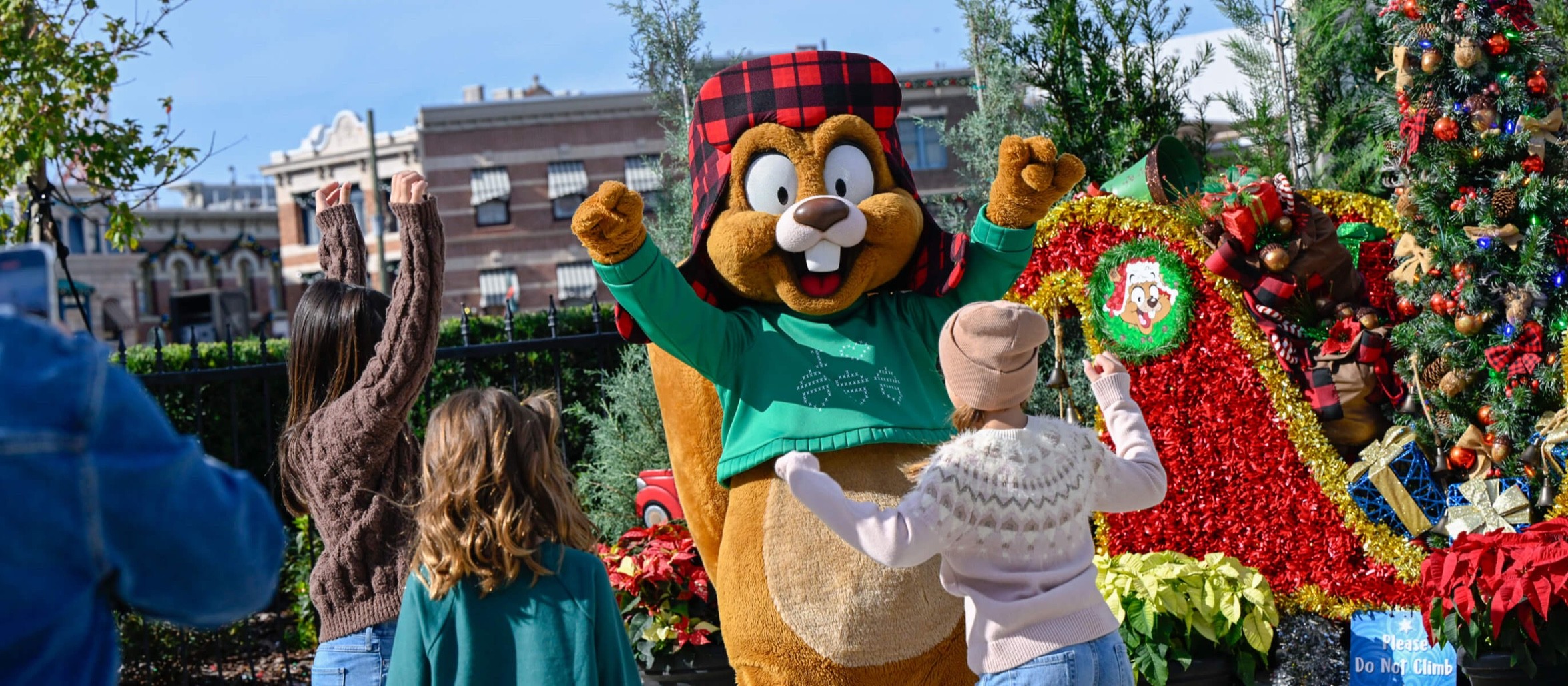 Kids cheering and dancing with Earl the Squirrel beside a decorated Christmas tree