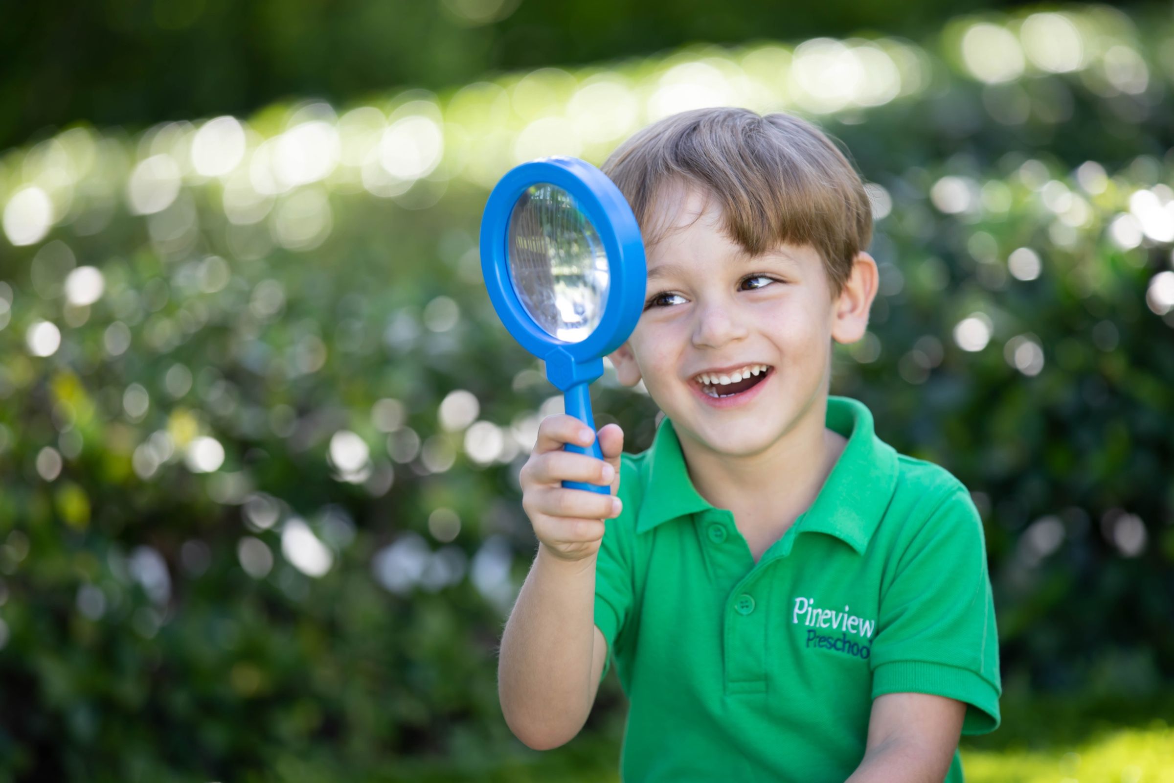 Un niño de preescolar explorando al aire libre con una lupa en Pineview Preschools