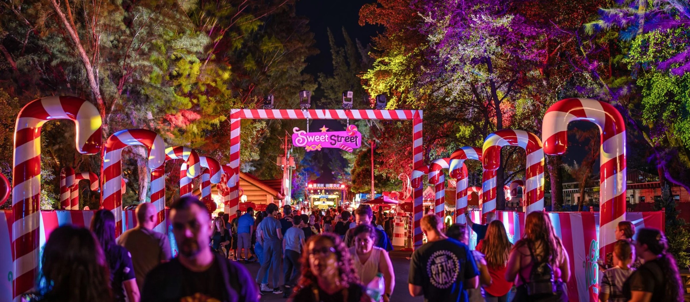 Crowds walking under giant candy-cane arches and colorful lights on Sweet Street at Christmas Wonderland
