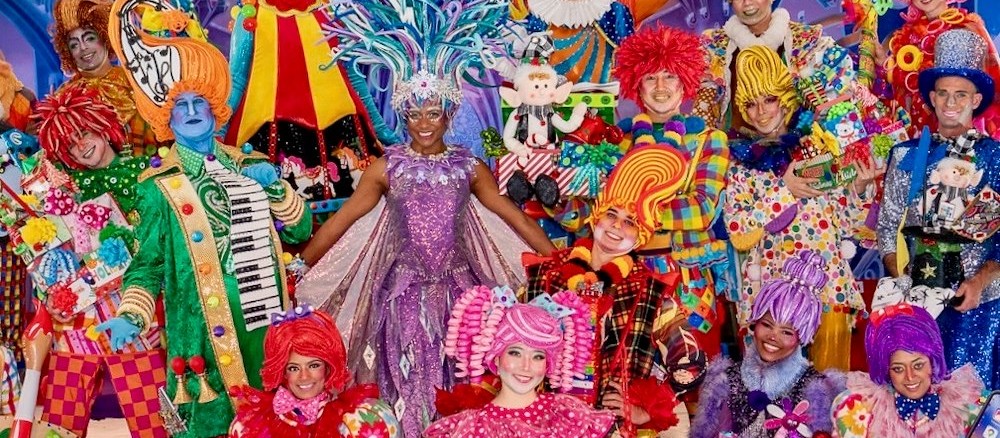 The show's cast in bright, candy-colored costumes posing together on stage