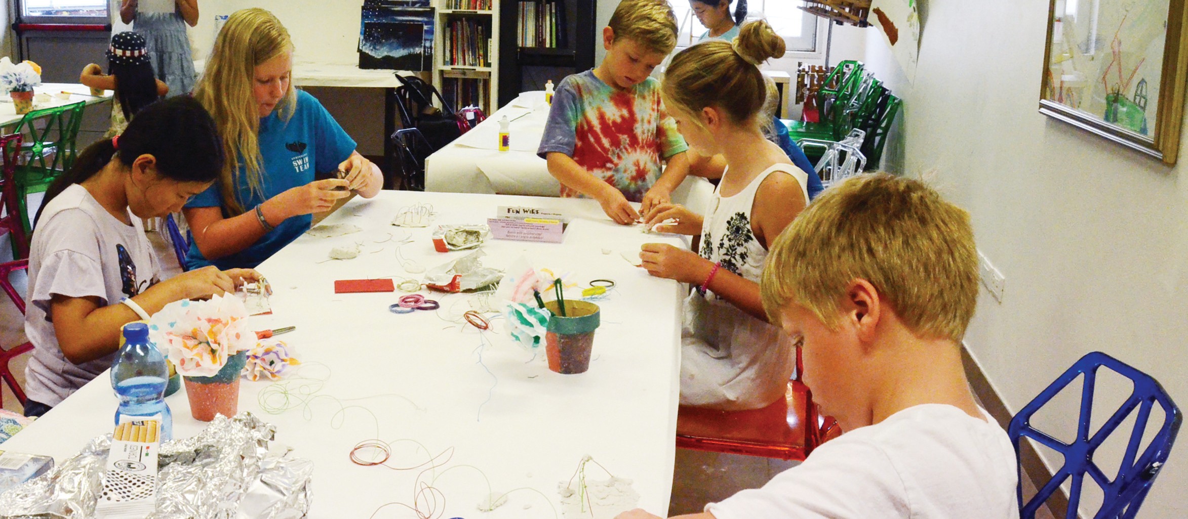 Children making crafts around a long table covered with supplies