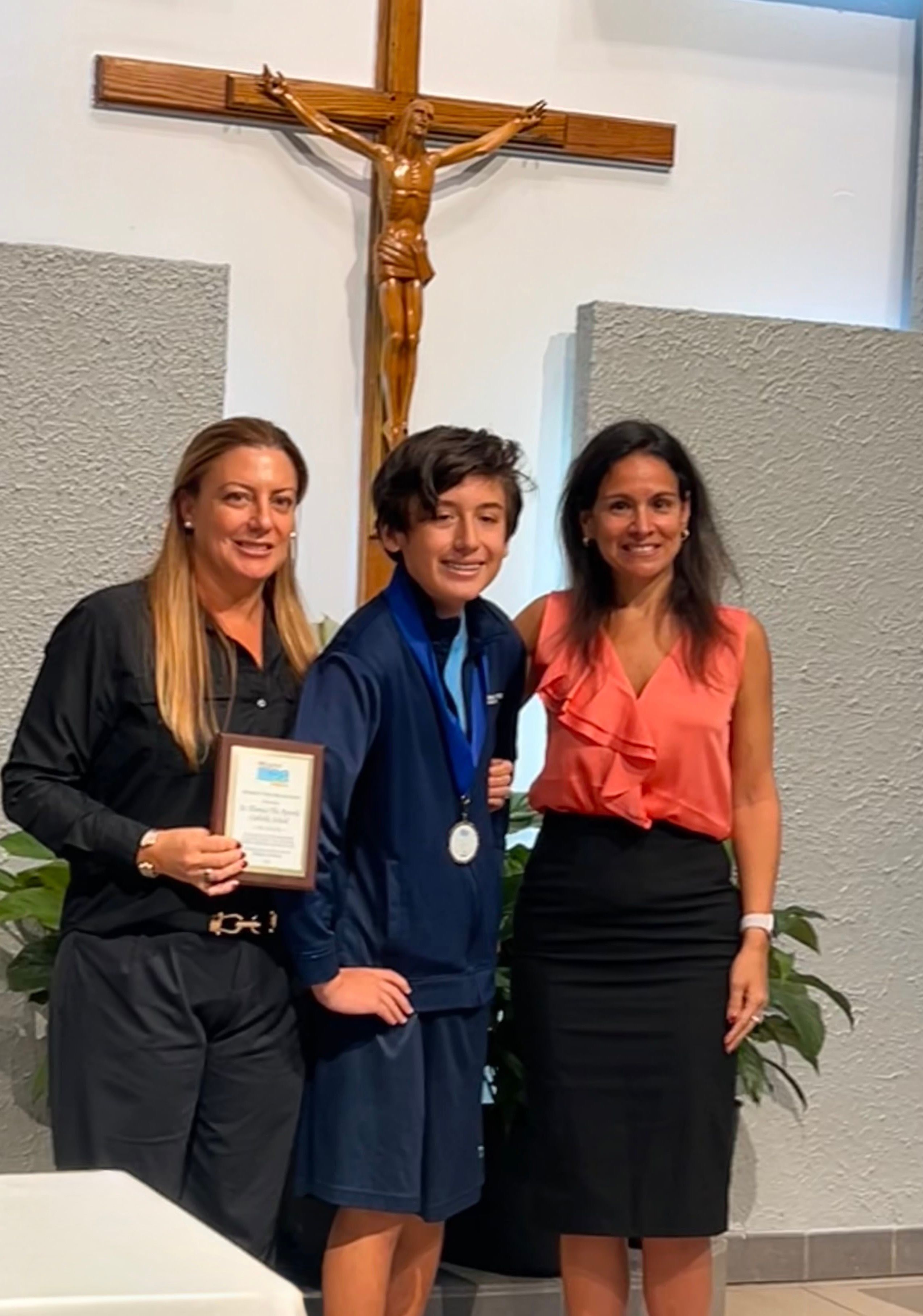 Un estudiante con medalla y placa entre dos mujeres en una ceremonia de premios escolar