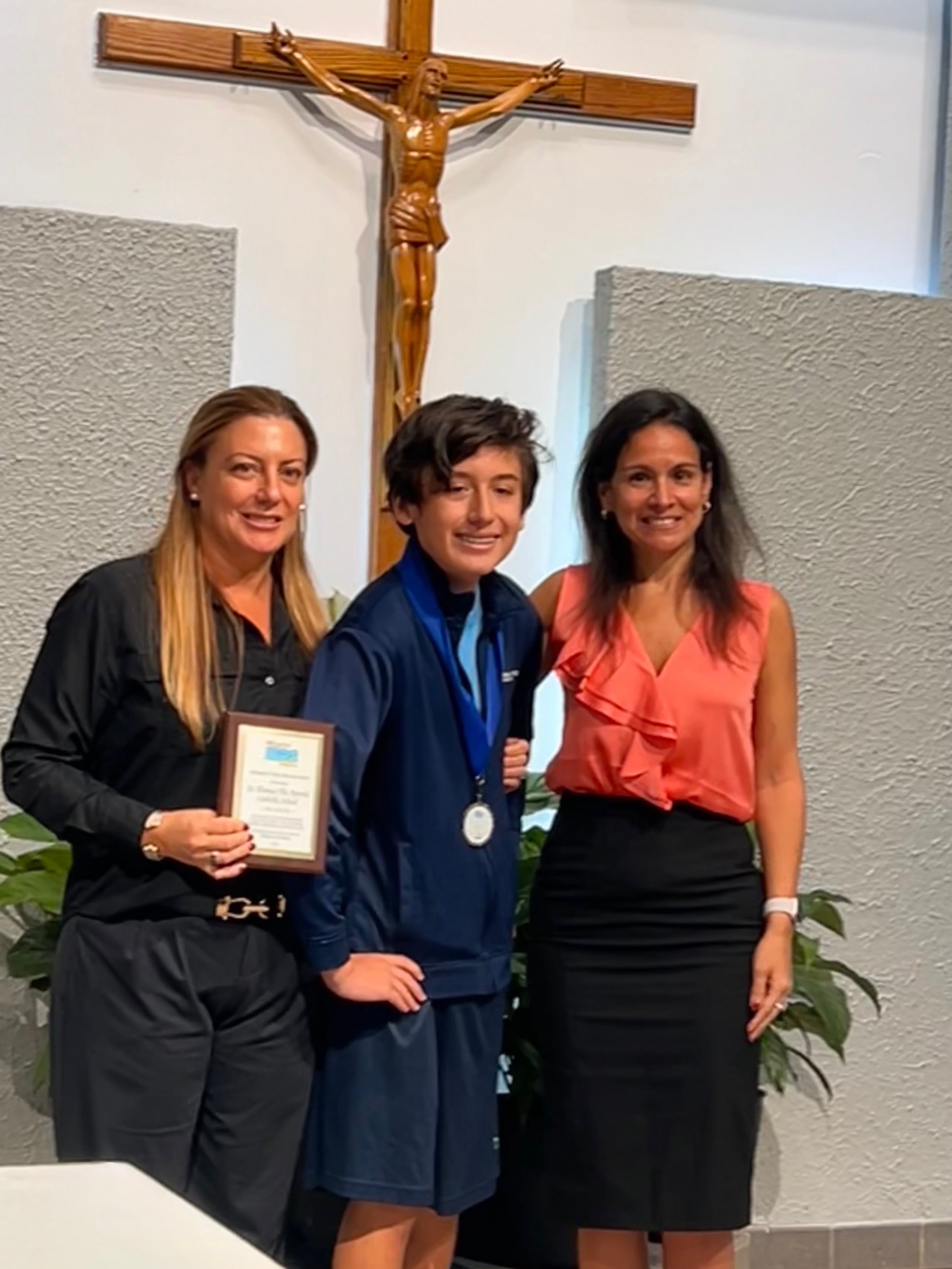 Un estudiante con medalla y placa entre dos mujeres en una ceremonia de premios escolar