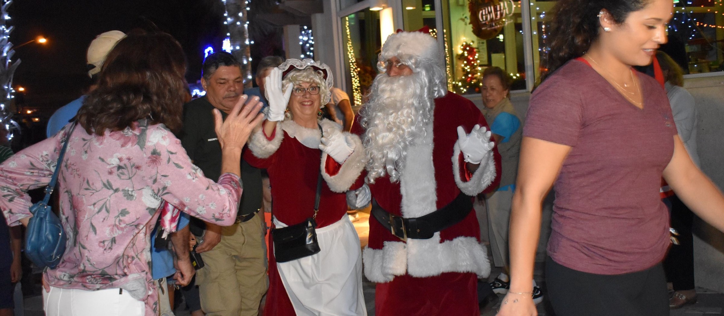 Santa and Mrs. Claus high-fiving families in the crowd at night