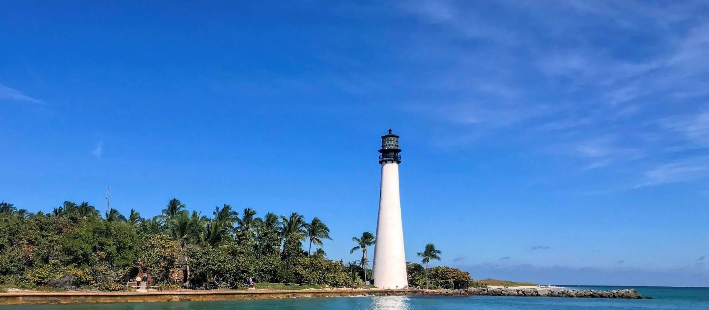 A white lighthouse on a palm-lined point across the blue water of Biscayne Bay