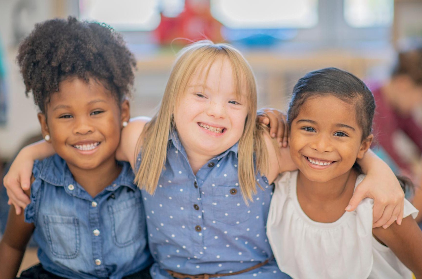 Three smiling girls with their arms around each other in a classroom