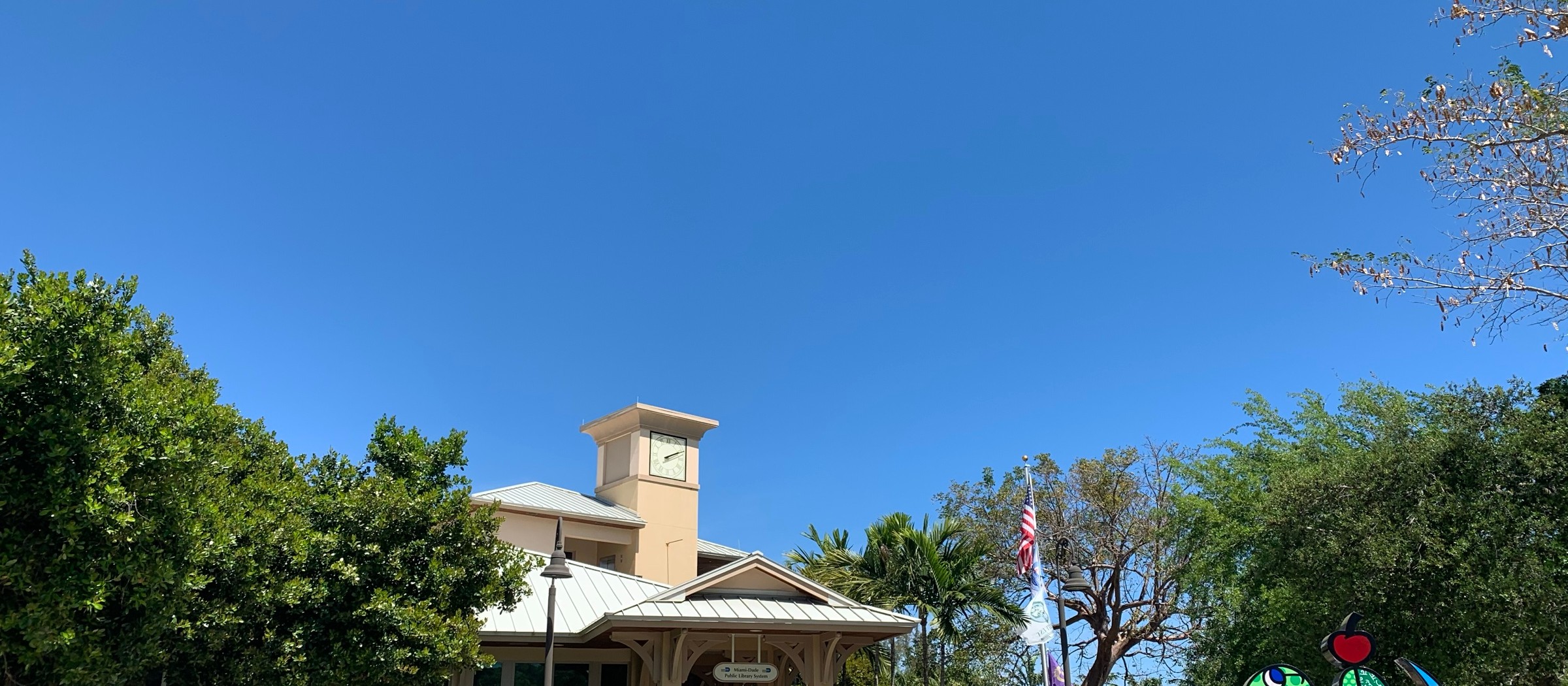 El edificio de la biblioteca de Palmetto Bay y su jardín delantero bajo un cielo azul
