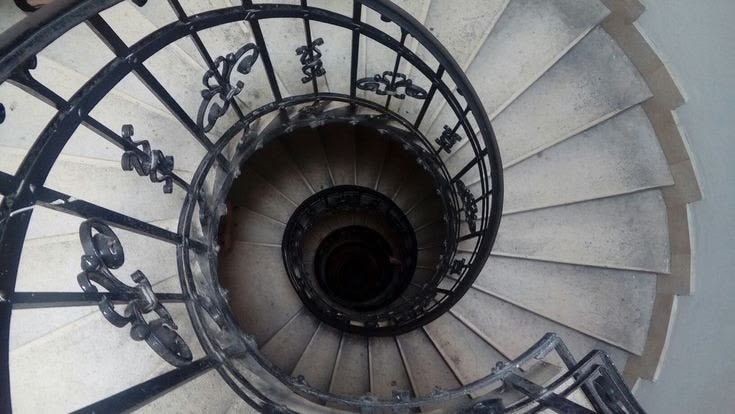 A spiral stone staircase with an ornate iron railing, viewed from above.