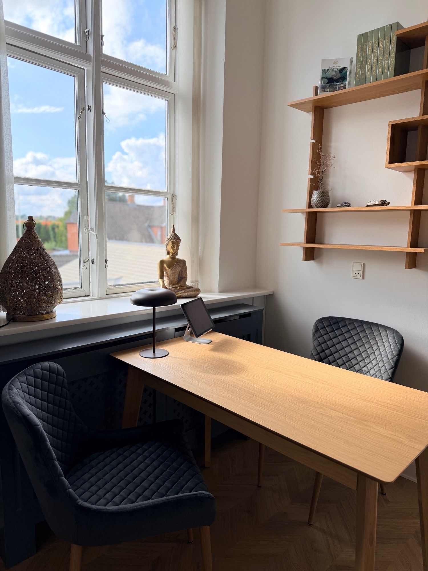 Konsultationsbord ved vinduet med Buddha-figur og træhylder