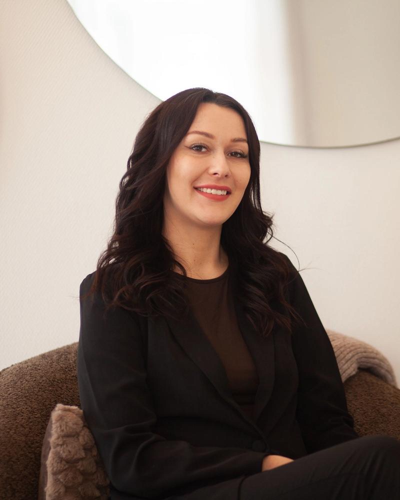 Camilla Madsbøll i sort blazer smiler i en lænestol