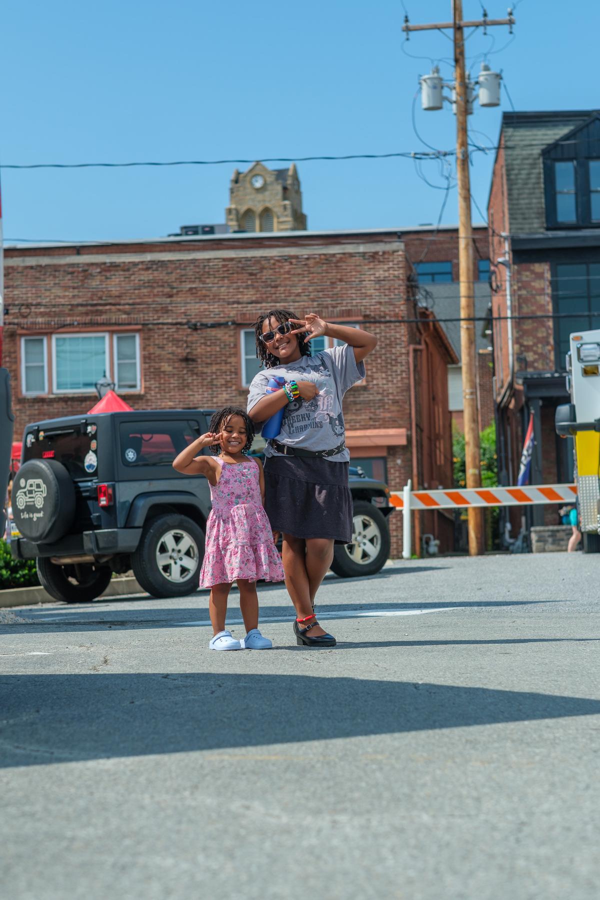 Cori and Charlie mid street, both throwing hand signs, clock tower behind them.