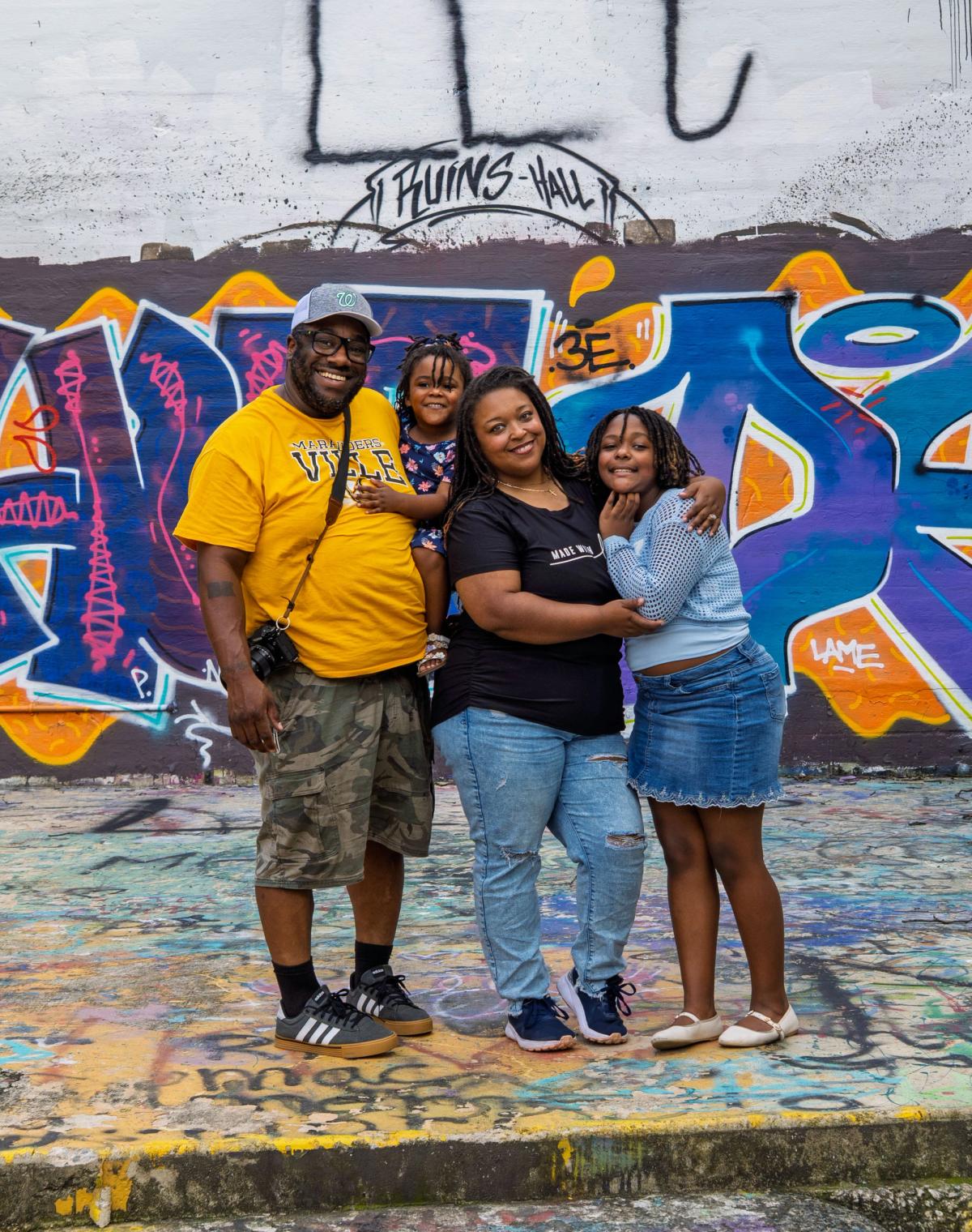 Mark with his wife, Cori and Charlie at The Ruins in Glen Rock, a camera still hanging off his shoulder, a graffiti wall behind them with RUINS HALL painted above. Photograph by Matt.