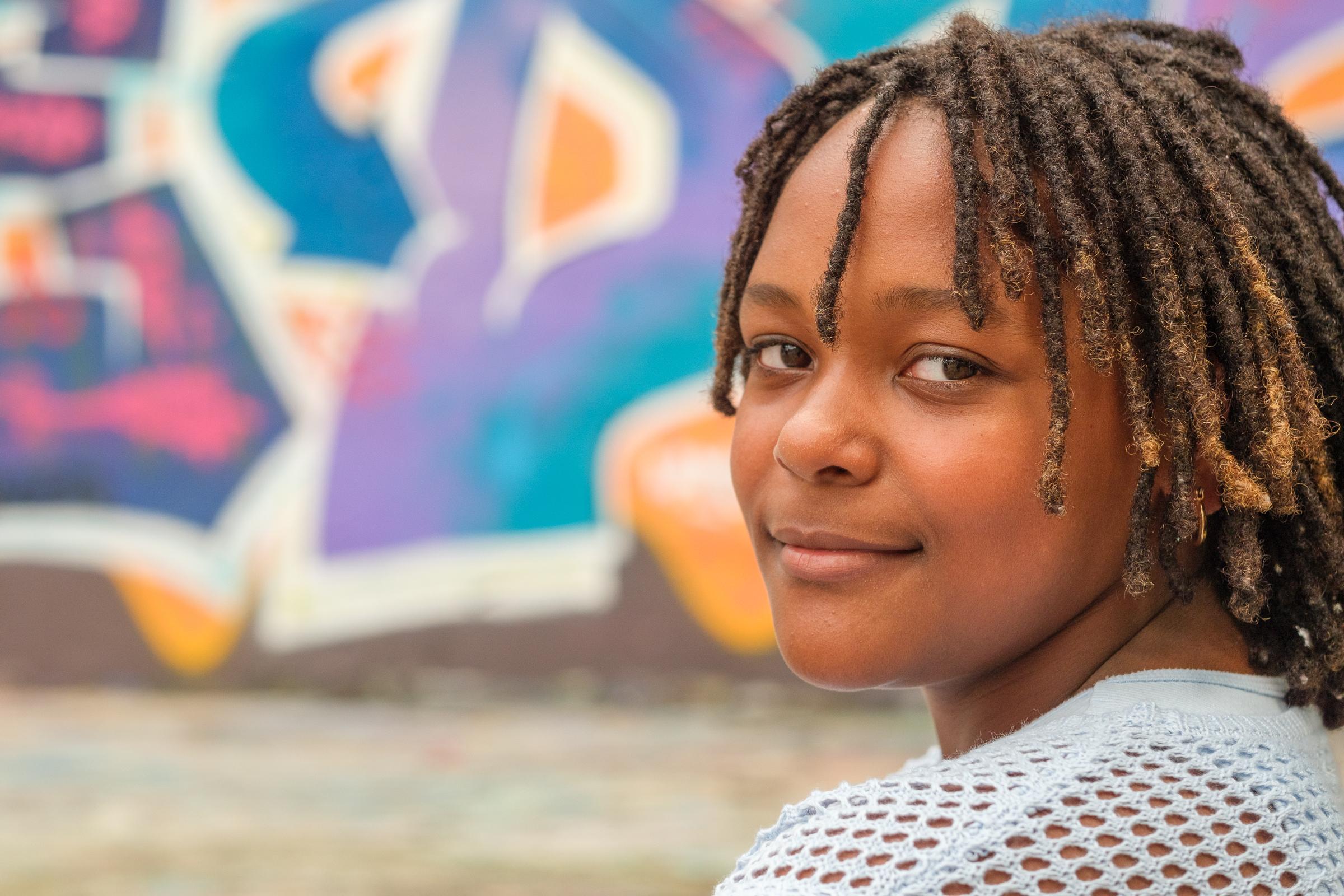 Cori close up looking to camera, a purple, blue and orange mural blurred behind her.