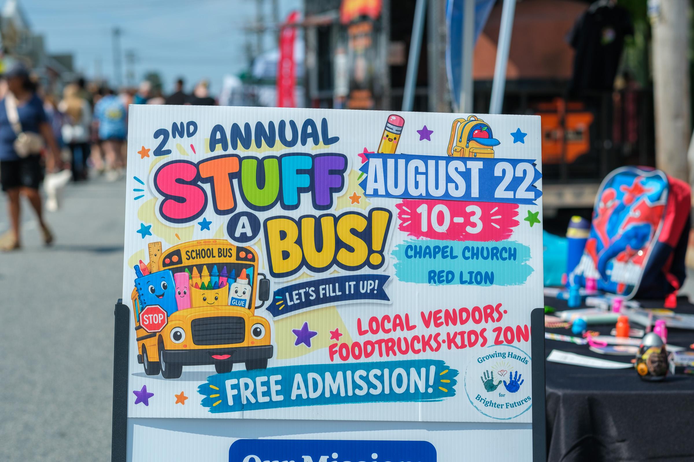 The Stuff-A-Bus A-frame sign with backpacks stacked behind it.