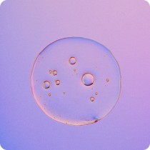 Close-up of a translucent liquid droplet with multiple small bubbles inside, set against a gradient purple and pink background.