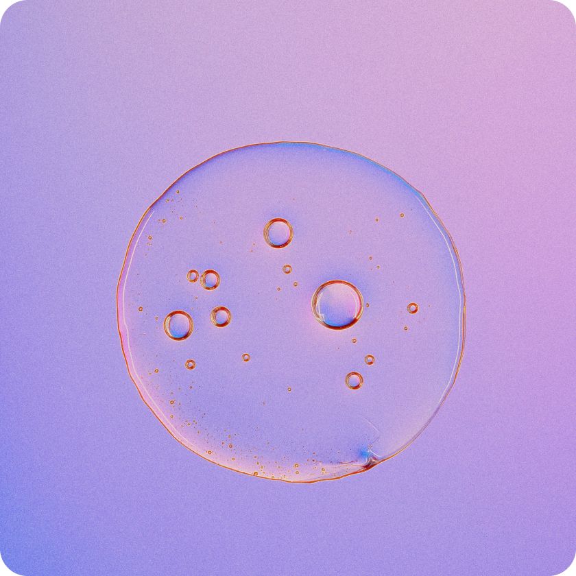 Close-up of a translucent liquid droplet with multiple small bubbles inside, set against a gradient purple and pink background.