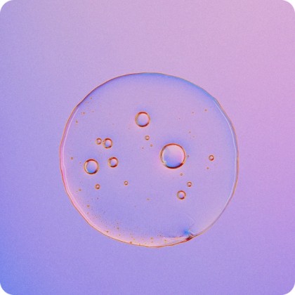 Close-up of a translucent liquid droplet with multiple small bubbles inside, set against a gradient purple and pink background.