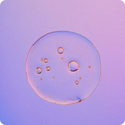 Close-up of a translucent liquid droplet with multiple small bubbles inside, set against a gradient purple and pink background.