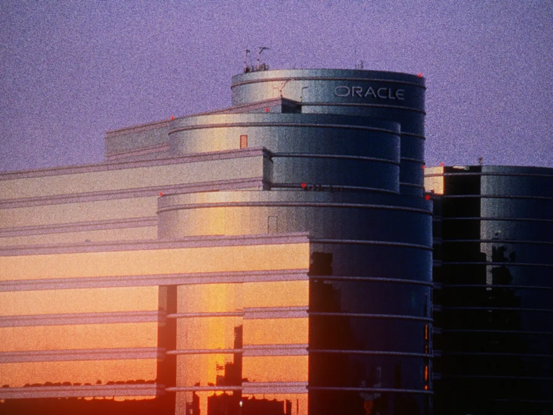 Modern glass building with curved structure reflecting sunset colors, labeled with the word "ORACLE" at the top.