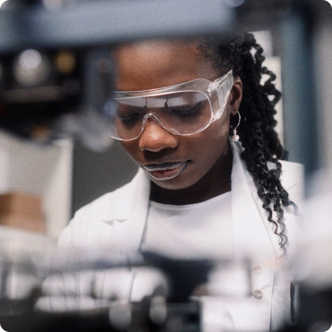 Scientist wearing safety goggles and a lab coat working in a laboratory, focused on equipment in front of her.