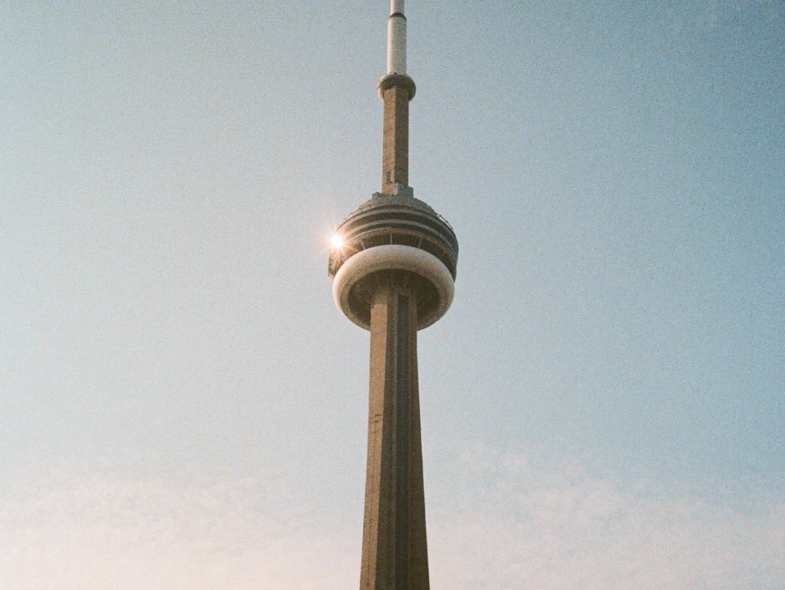 View of the CN Tower in Toronto rising into a clear sky, with sunlight reflecting off the observation deck near the top.