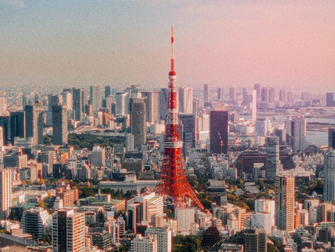 Aerial view of Tokyo Tower surrounded by skyscrapers during sunset, with a colorful sky in the background.