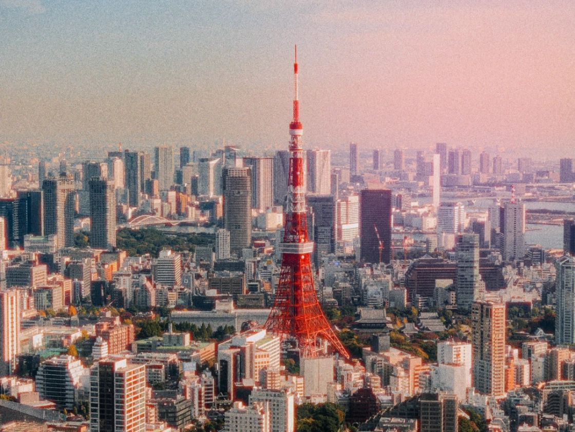 Aerial view of Tokyo Tower surrounded by skyscrapers during sunset, with a colorful sky in the background.