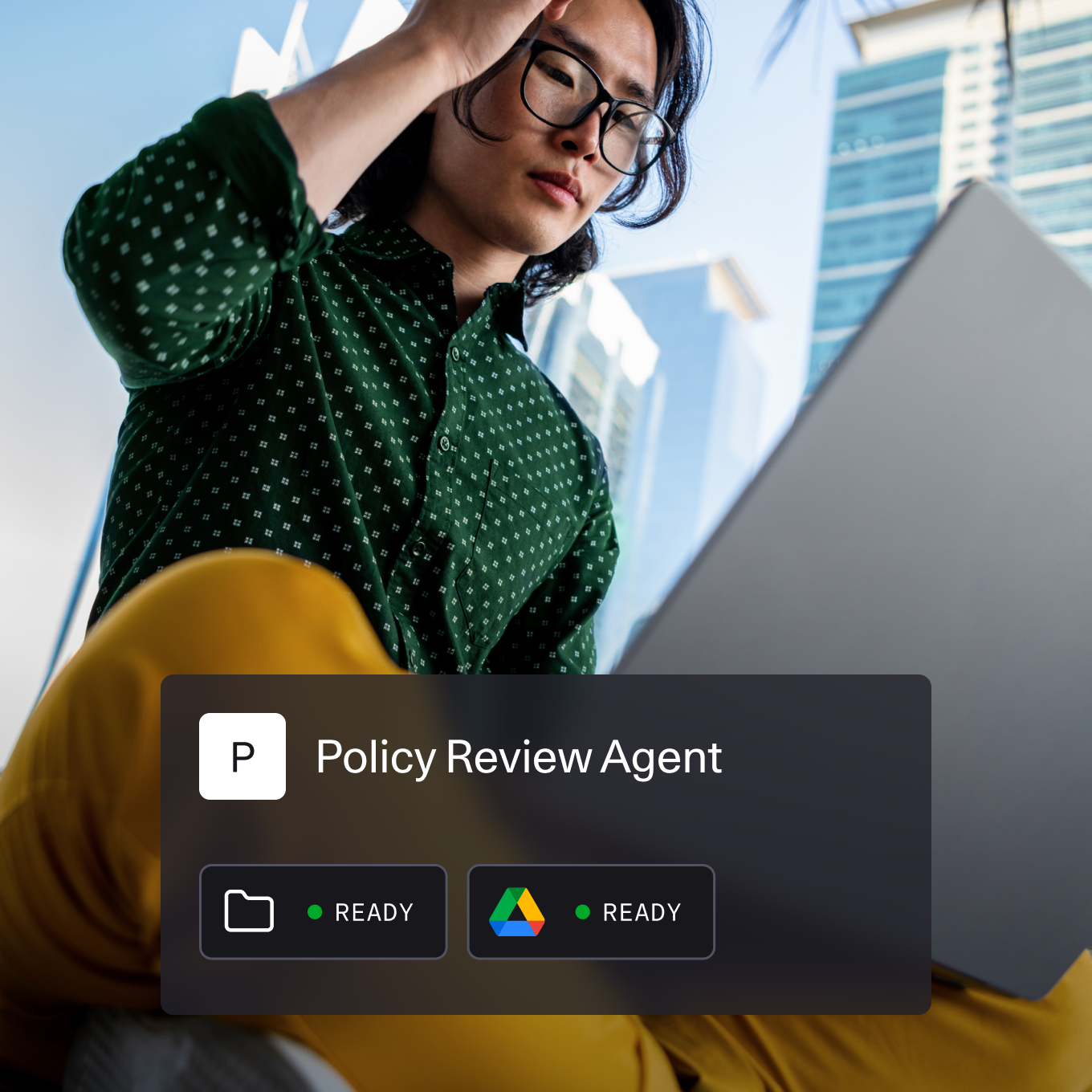 A person wearing a green patterned shirt and yellow pants is working on a laptop outdoors in an urban environment with tall glass buildings in the background. Overlaid on the image is a digital interface titled "Policy Review Agent" with icons indicating folder and Google Drive access, both marked as "READY."