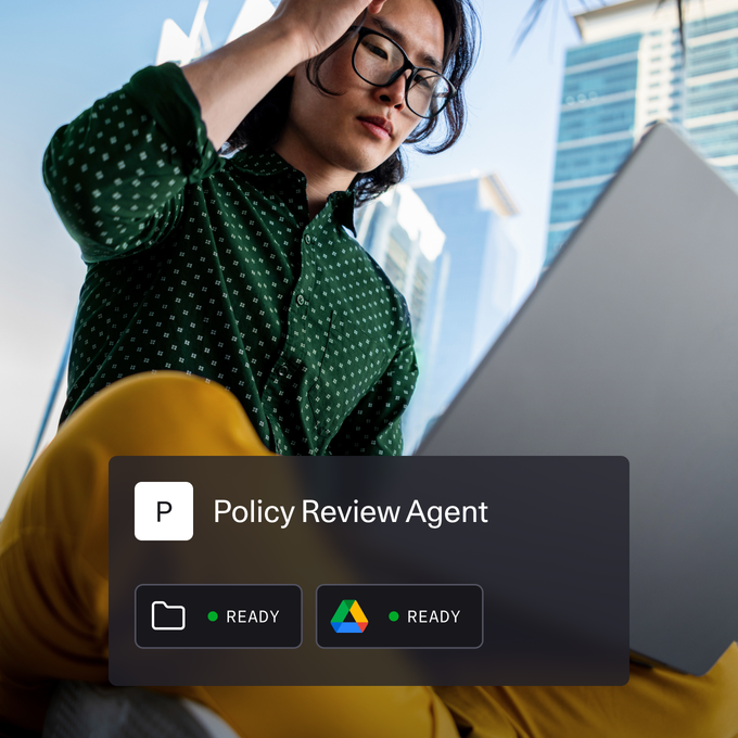A person wearing a green patterned shirt and yellow pants is working on a laptop outdoors in an urban environment with tall glass buildings in the background. Overlaid on the image is a digital interface titled "Policy Review Agent" with icons indicating folder and Google Drive access, both marked as "READY."