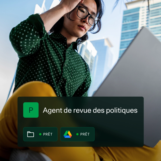 Une personne portant une chemise verte à motifs et un pantalon jaune travaille sur un ordinateur portable en plein air dans un environnement urbain avec de grands bâtiments en verre en arrière-plan. Superposée à l’image, une interface numérique indique « Agent d'analyse des politiques » avec des icônes indiquant l'accès à un dossier et à Google Drive, tous deux indiquant PRÊT.