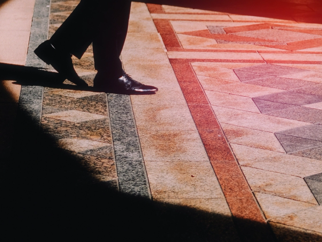 A well-dressed person in a suit and tie strides purposefully on a tiled surface.