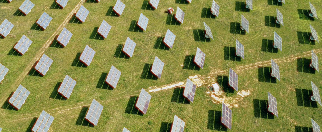 Aerial view of a solar farm with rows of solar panels on green grass. The orderly panels cast shadows, creating a pattern of sustainability and innovation.