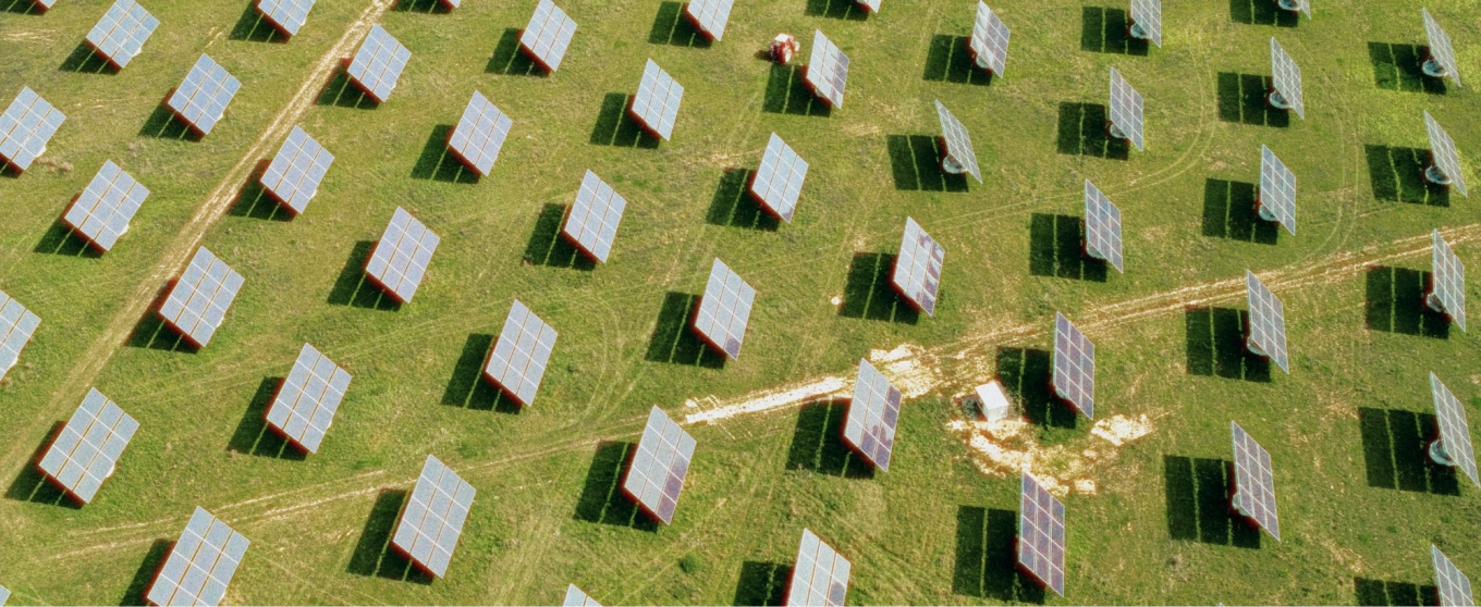 Aerial view of a solar farm with rows of solar panels on green grass. The orderly panels cast shadows, creating a pattern of sustainability and innovation.