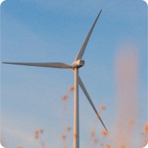 Close-up of a wind turbine against a clear blue sky, with blurred plants in the foreground.