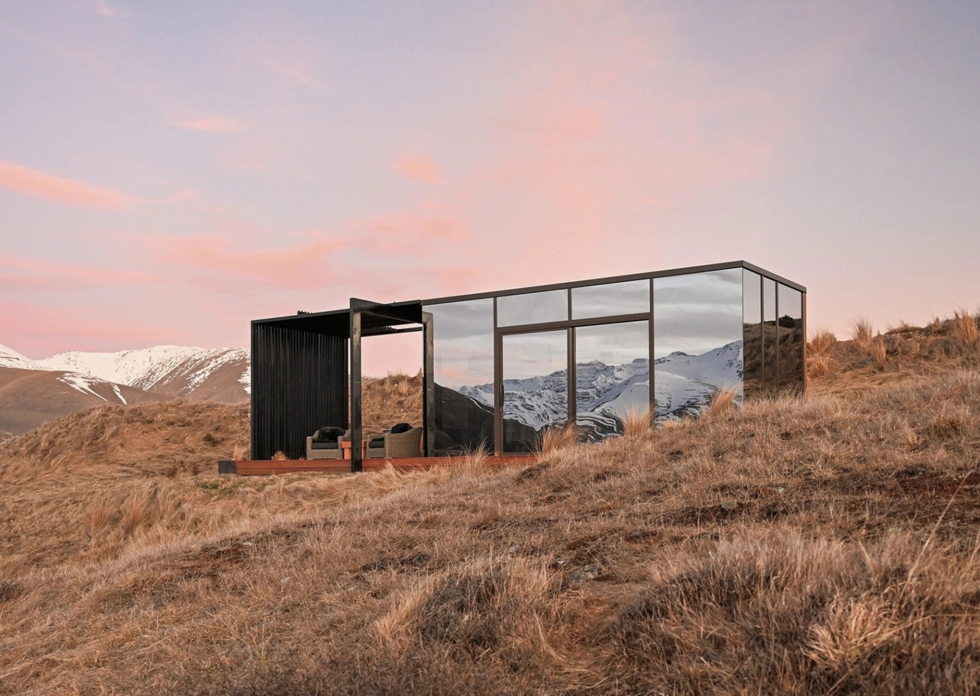 A mirrored cabin in golden tussock beneath the Southern Alps