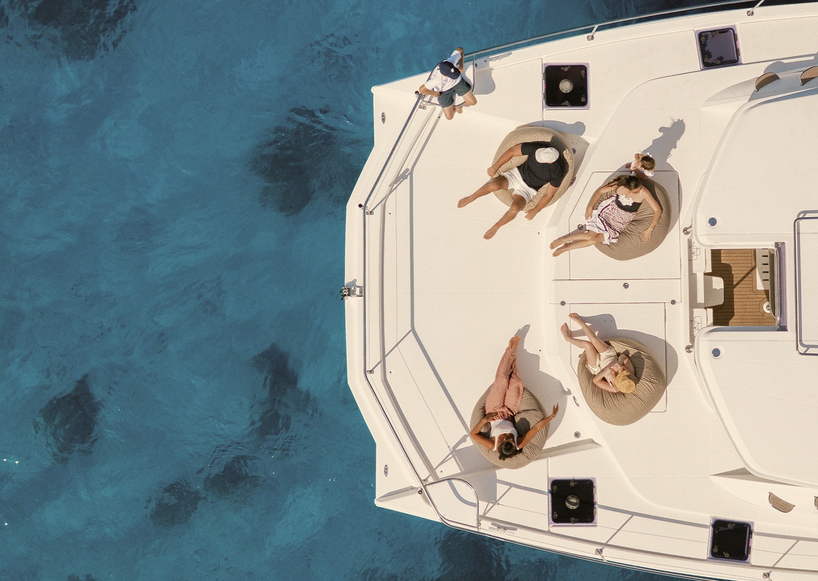 Guests relax on the deck of a catamaran above clear blue water
